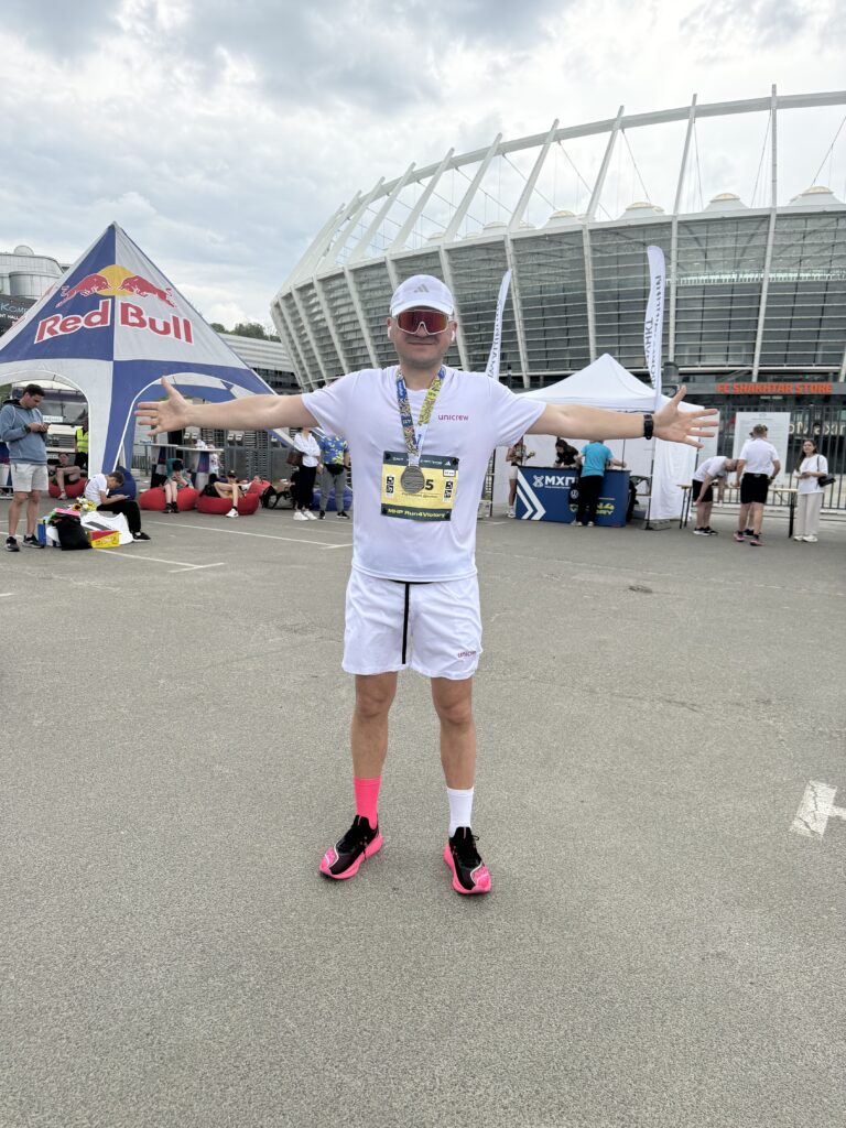 Dmytro Reutskyi wearing his marathon finisher's medal and a unicrew shirt outside the stadium in Kyiv